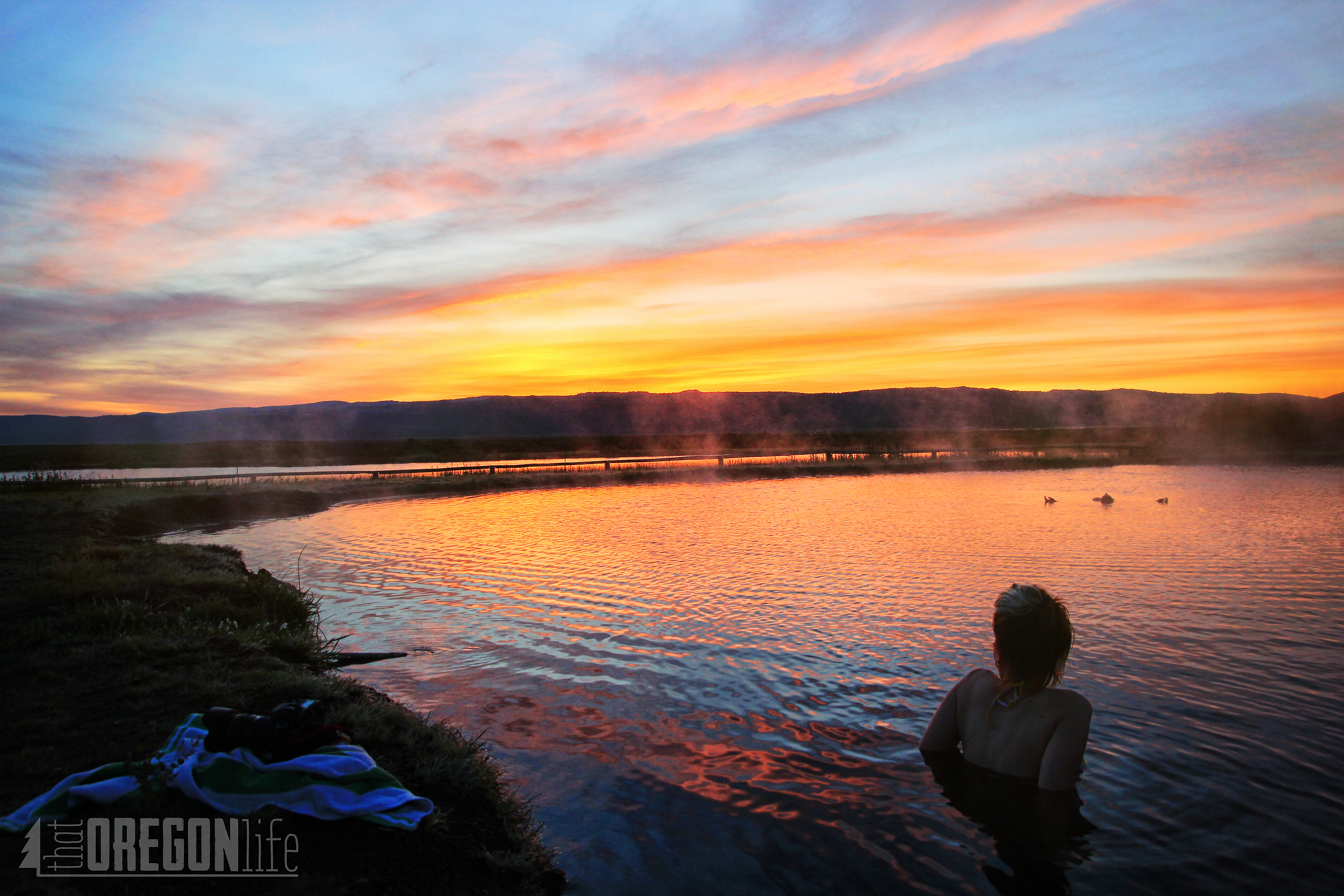 A woman soaks in the hot springs at sunset in the high desert.
