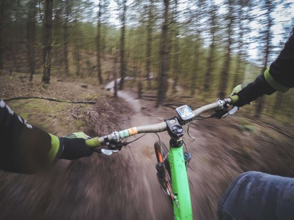 A mountain biker goes down a trail through the woods on a bright green mountain bike.