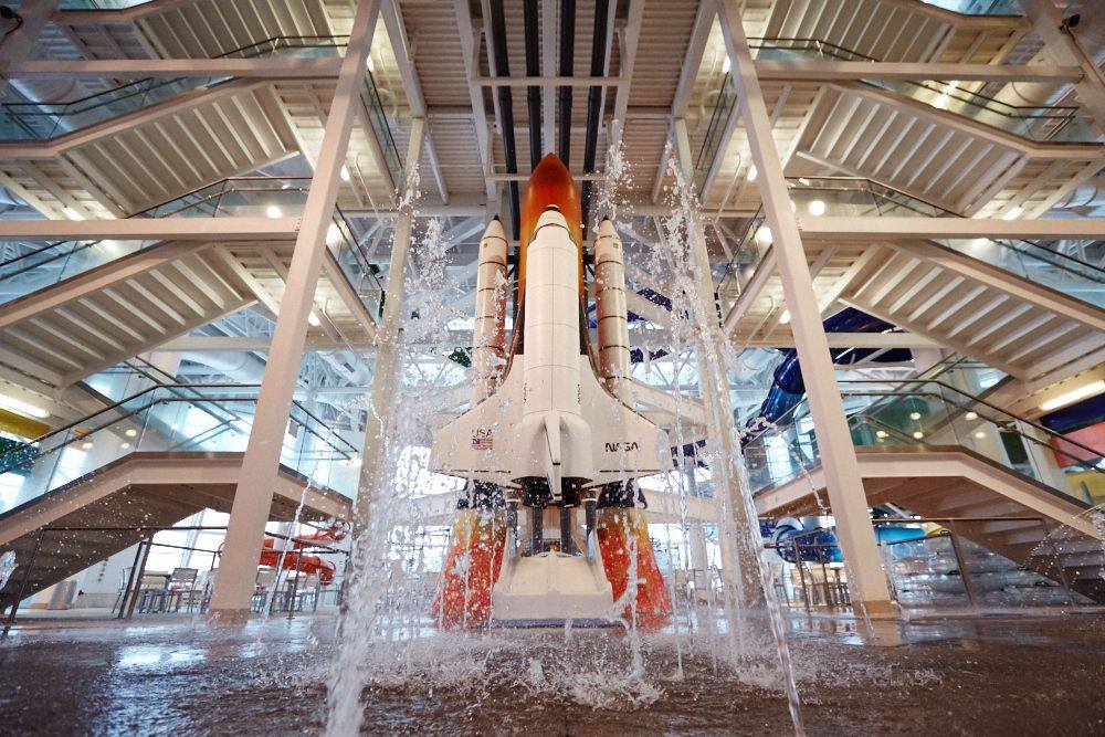 A replica of the Nasa Shuttle inside the Wings And Waves Waterpark with fountains shooting up in front of it.