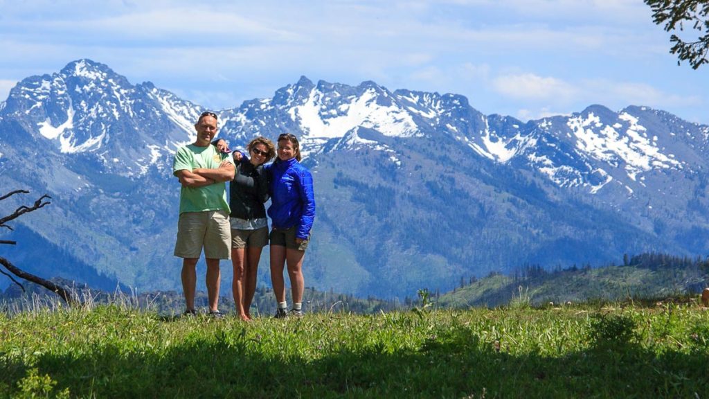Three people stand at an overlook with snowy mountains in the background.