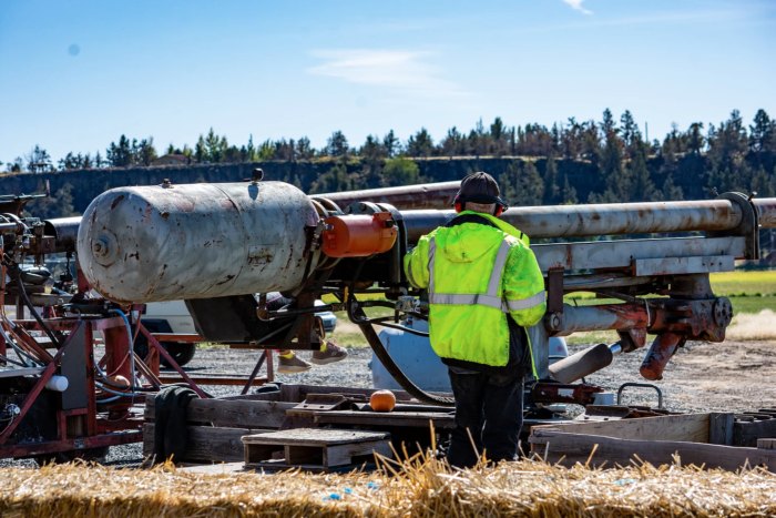 A man operates a pumpkin canon at Smith Rock Ranch.  He's wearing a bright yellow safety coat.