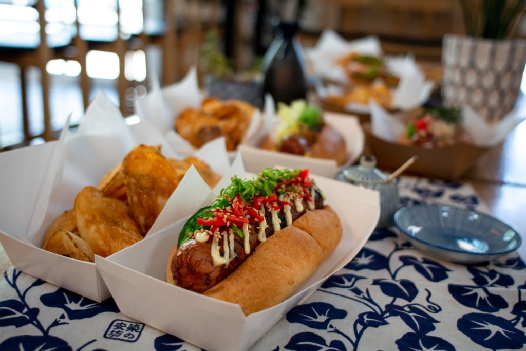 A delicious looking Kemuri Japanese hotdog with toppings and fresh chips in Portland Oregon.