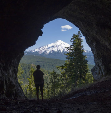 A man in a cave looks out at Mt Jefferson in Oregon.