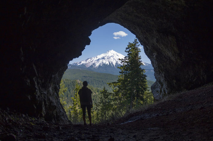 A man in a cave looks out at Mt Jefferson in Oregon.