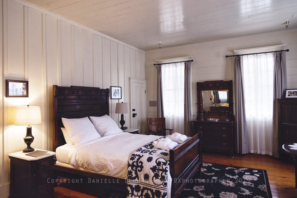 The interior of one of the rooms at the Wolf Creek Inn. There's a large bed with black and white bedding, and white wood walls.