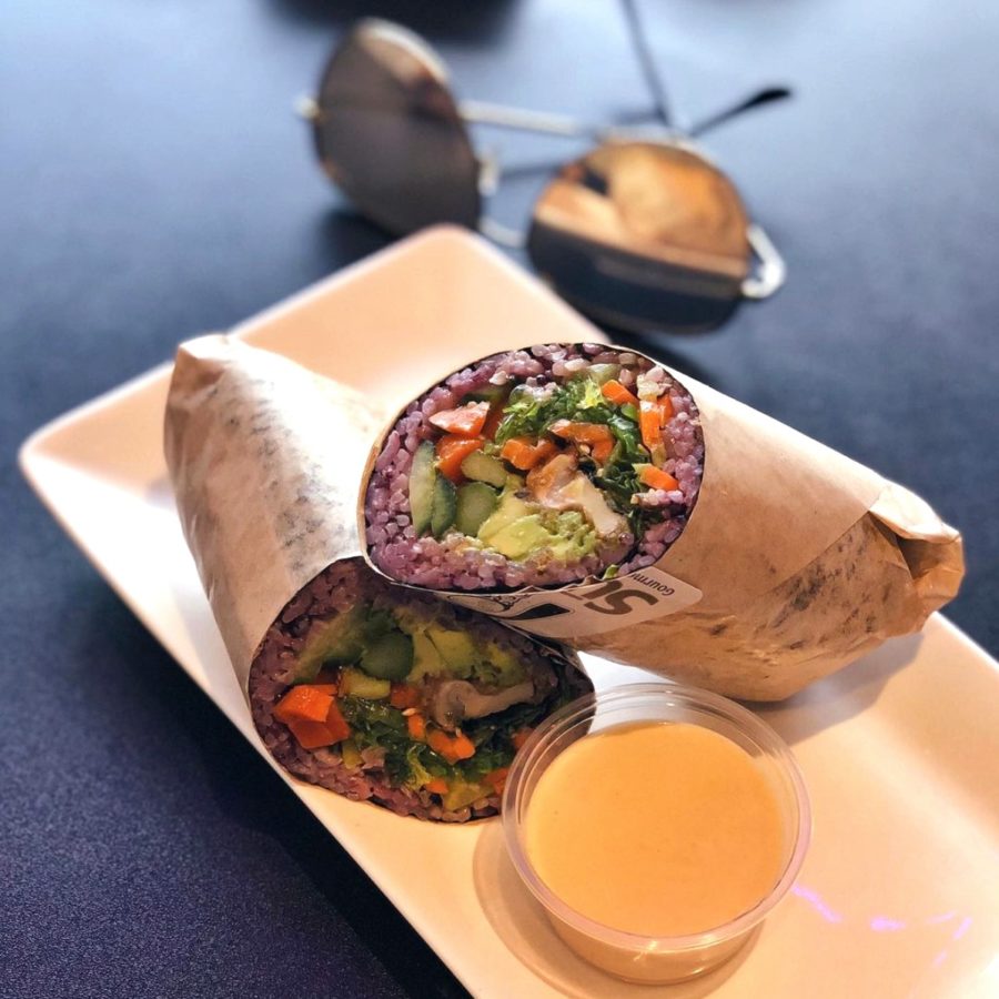 a sushi burrito arranged on a wood platter with dipping sauce