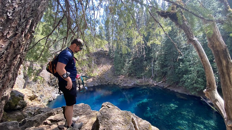 A man stands on rocks above blue pool at Tamolitch Falls. 