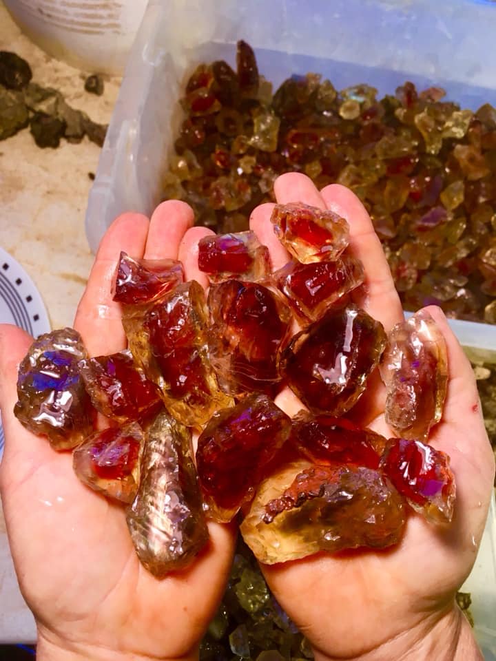 Someone holds a dozen very large deep red sunstones in their hands.