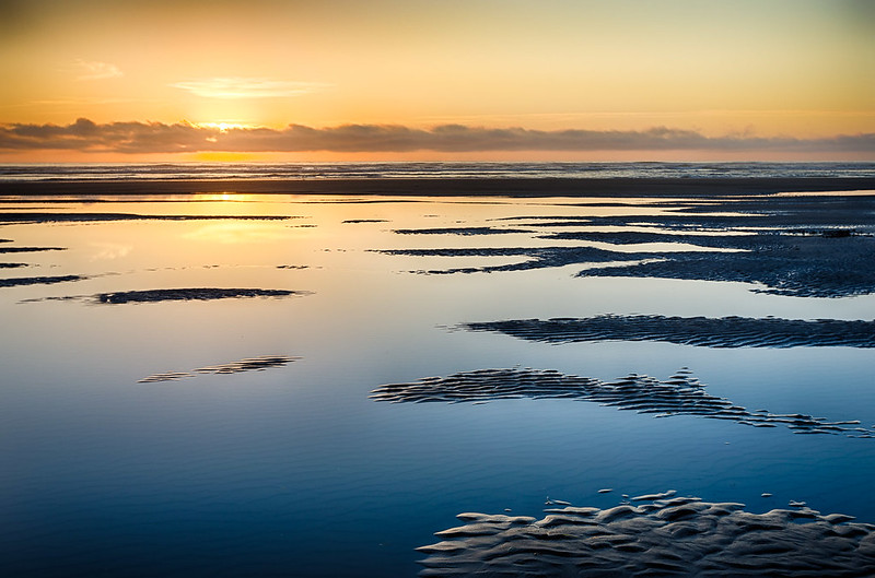 Seaside at sunset.  It's a view of the beach covered in water with the sunset reflecting off of the still waters.