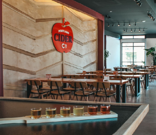 Portland Cider Co taproom tables with apple logo on the wall