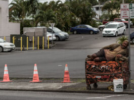 Homeless man sleeping on top of dumpster near sign in Portland Oregon