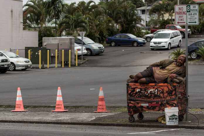Homeless man sleeping on top of dumpster near sign in Portland Oregon