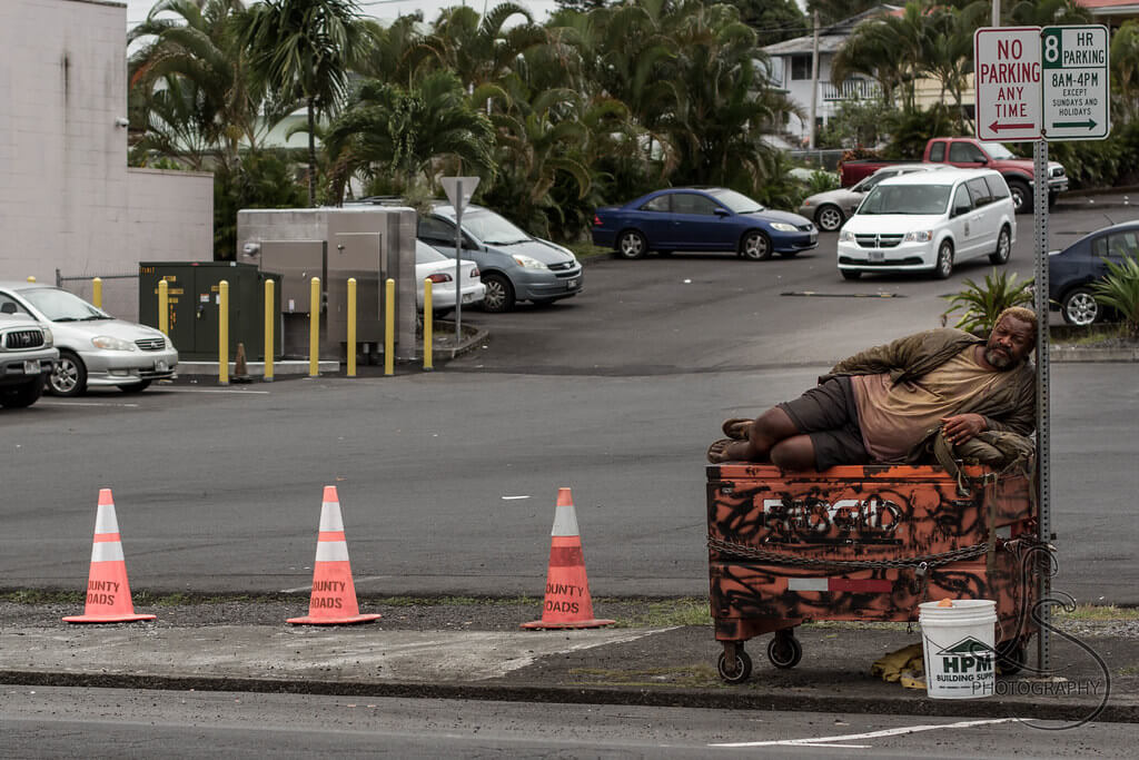 Homeless man sleeping on top of dumpster near sign in Portland Oregon