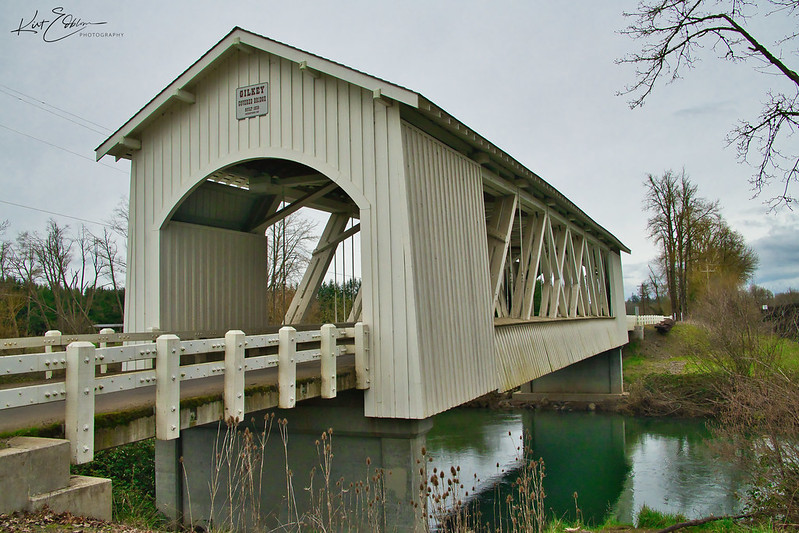 Gilkey Covered Bridge over the blue green water of Thomas Creek on a cloudy day in Oregon.