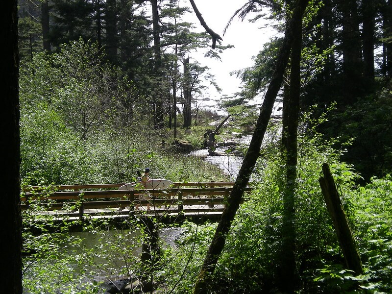 Surfer crossing bridge on forest trail near Manzanita Beach Oregon