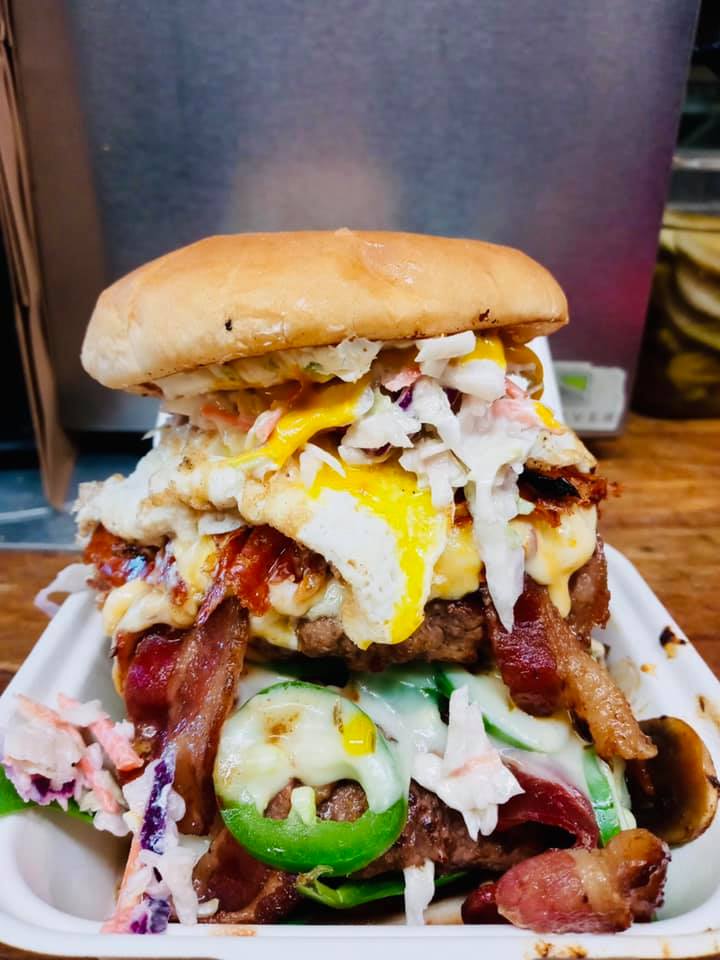 A burger stacked super high with toppings that looks impossible to eat without making a mess at Jasper's Cafe