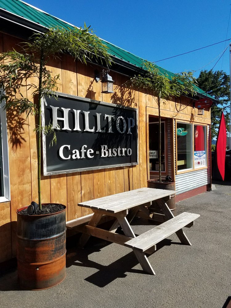 The outside of the Hilltop Cafe.  A picnic table in front of the Hilltop Cafe sign between two potted trees.