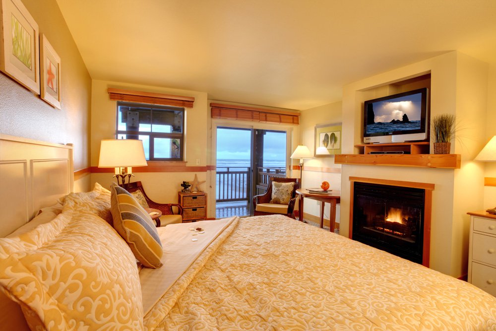 A cozy room with a big bed, ocean view, and a fireplace at The Ocean Lodge in Cannon Beach, Oregon.