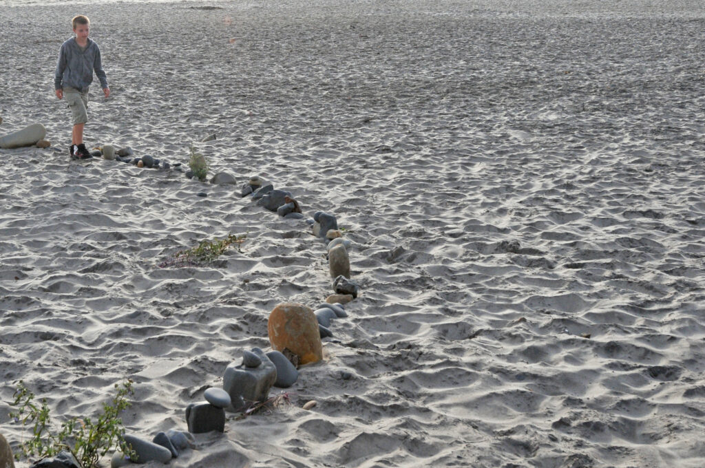 a boy walks in the sand with a line of agates on an oregon beach