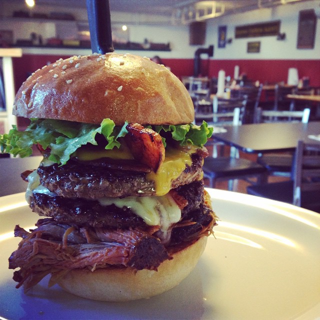 A super tall burger with two burger patties, pulled BBQ meat, cheese, lettuce and other toppings.