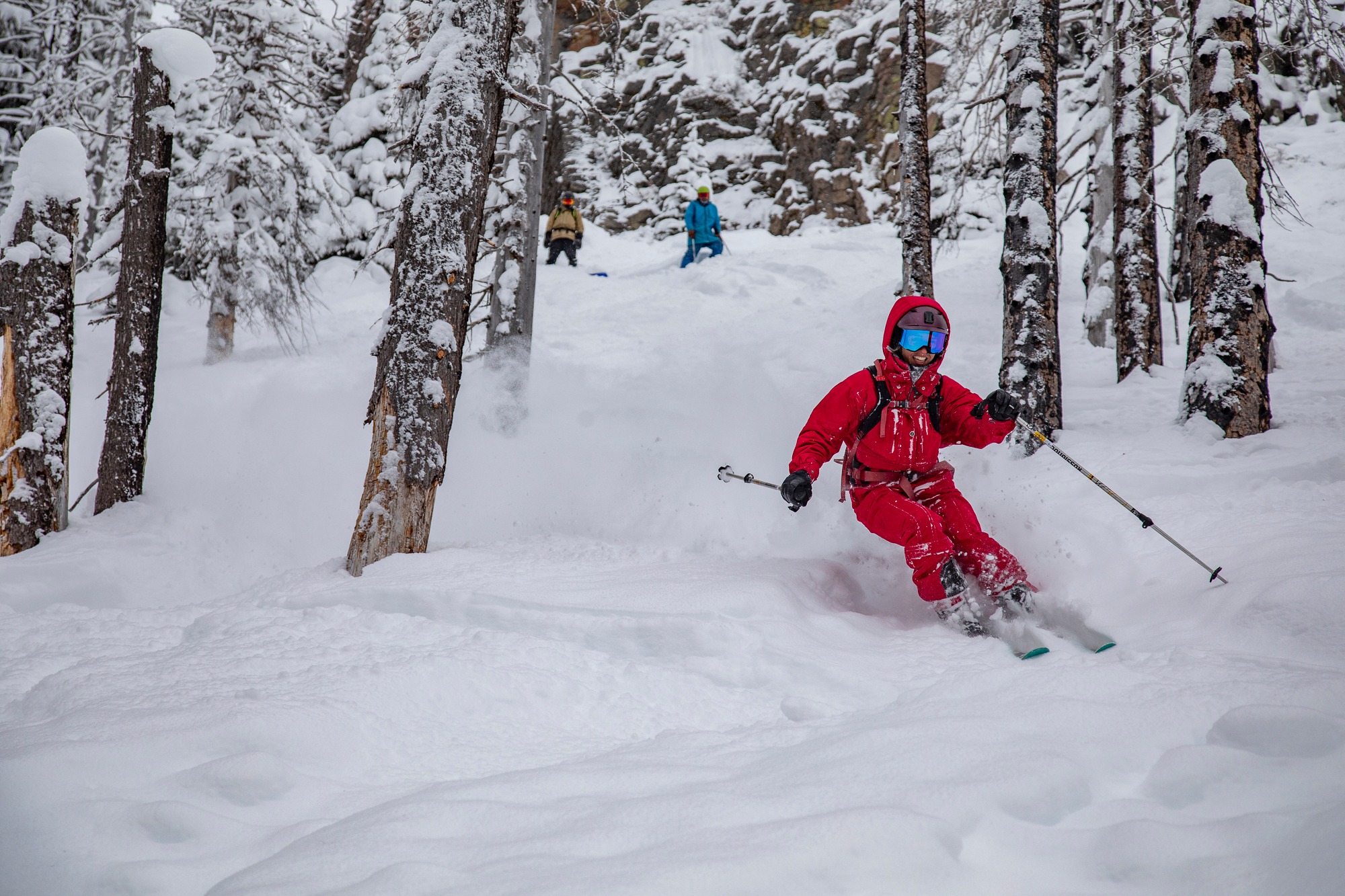 A person in red, and a person in blue skiing through the trees at Mount Hood Meadows.