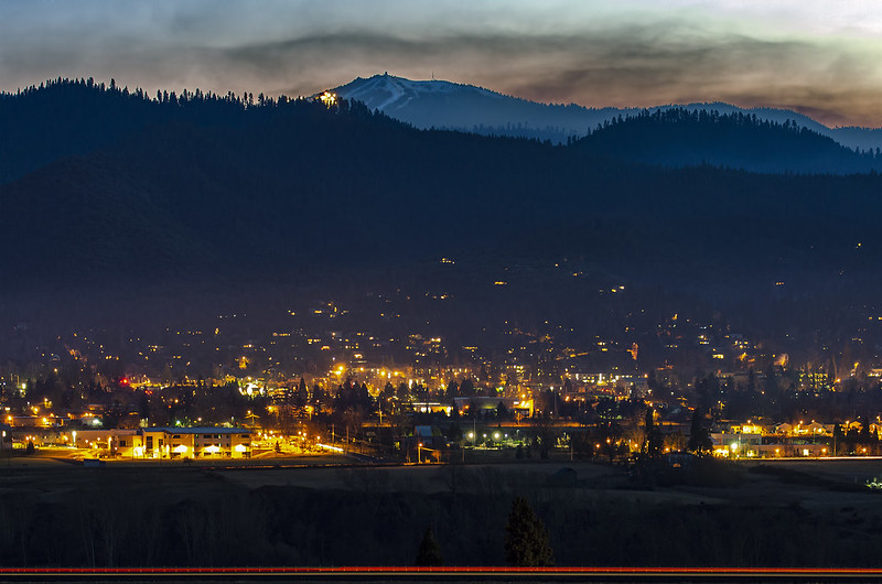 The city lights of Ashland at night with a mountain silhouetted in the background.