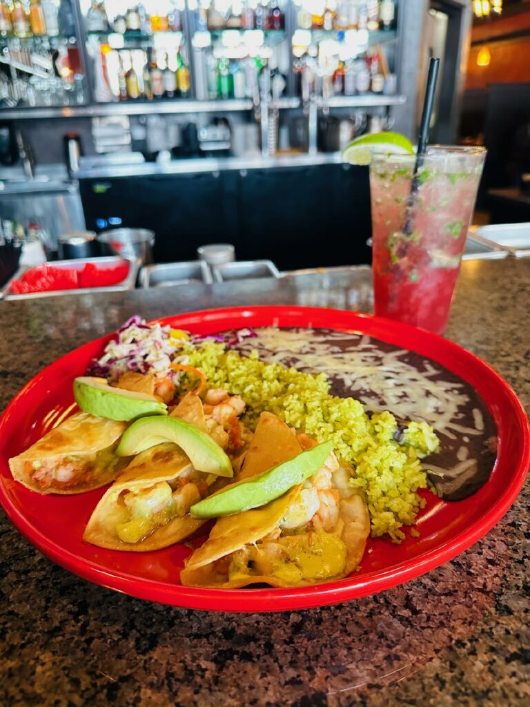 Tasty looking tacos on a red plate with a pink drink in the background.