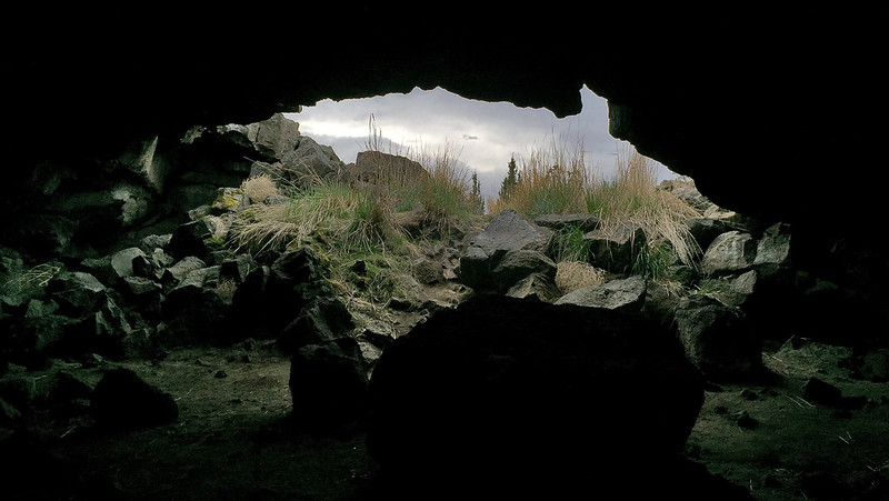 The view from inside one of the caves in Redmond. Tall grasses are just outside the mouth of the dark cave. Boulders are on the cave floor.