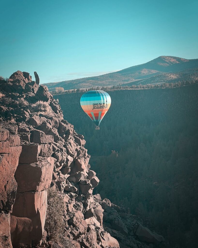 A blue and orange hot air balloon next to a rocky red cliff with a mountain in the background.