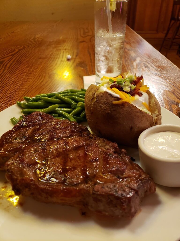 A delicious looking steak and potato with green beans.