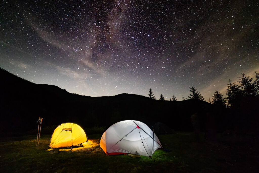 Two tents lit up at night under the stars in the wilderness.