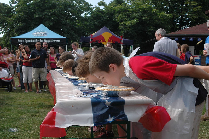 People lined up eating pies for a pie eating contest outside.