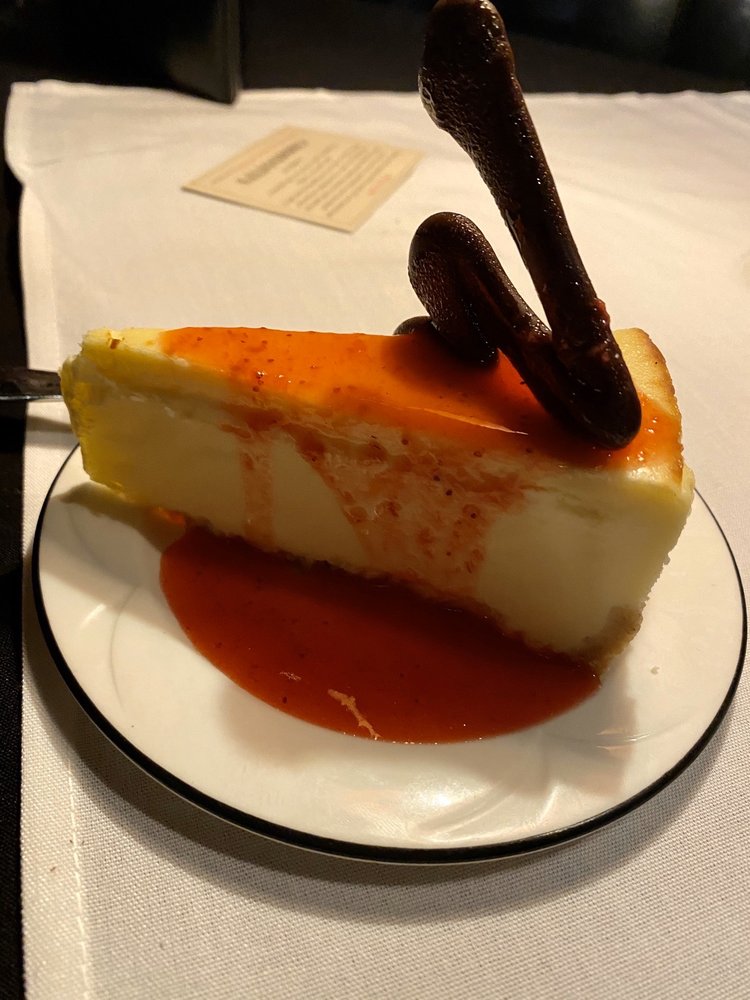 A white cheesecake covered in red sauce with a tall decorative piece of chocolate on top.