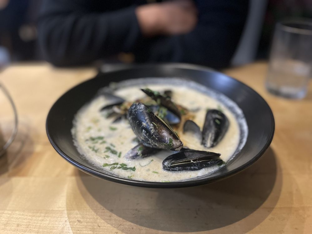 A black bowl filled with black muscles and coconut curry.