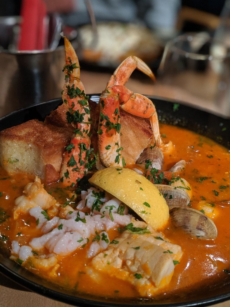 A red stew with crab sticking out and lemon. It looks delicious.