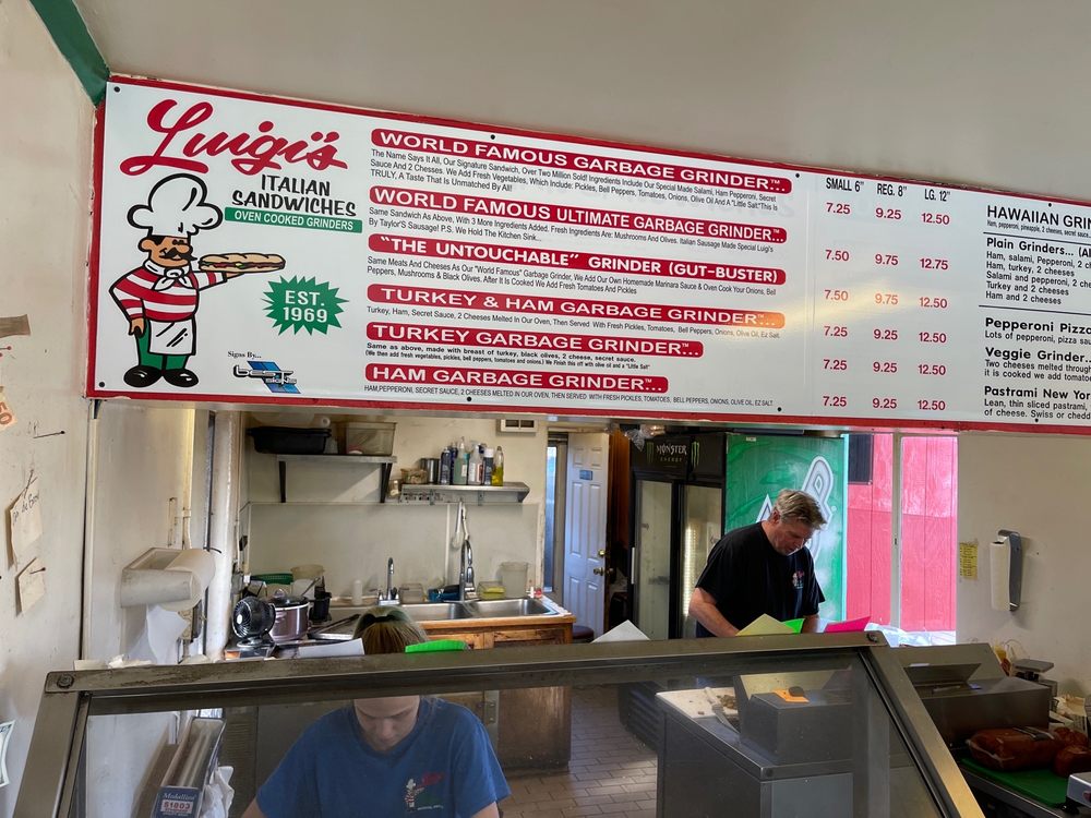 The menu hanging above the serving counter. Two people are in the back preparing sandwiches.