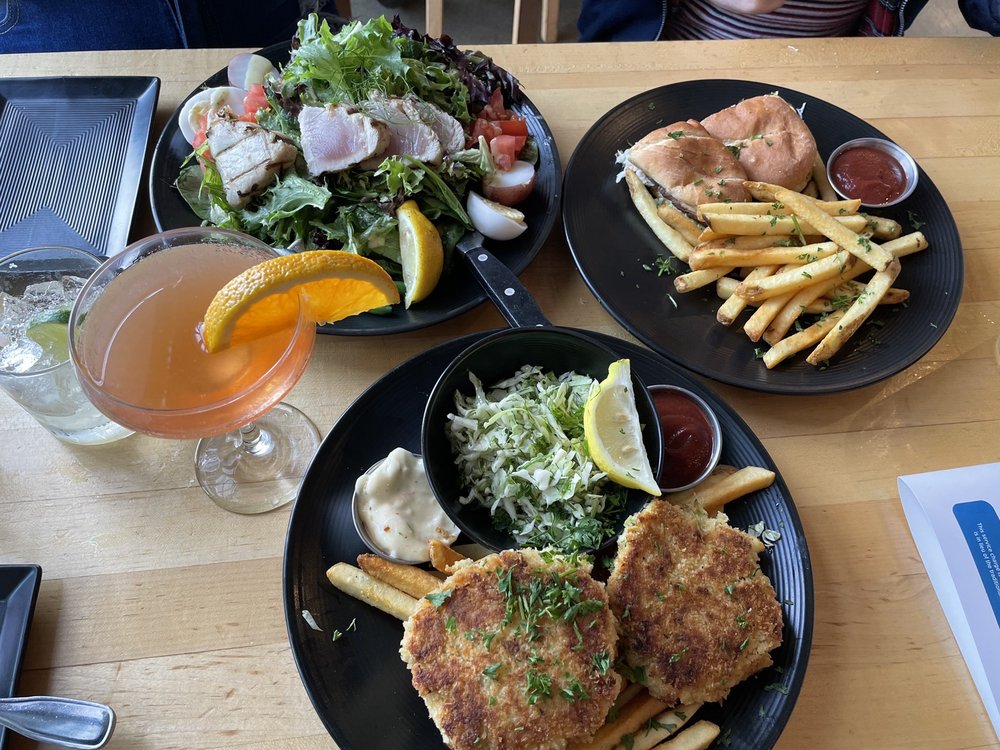 A table full of various plates of food including nicoise salad and crab cakes.