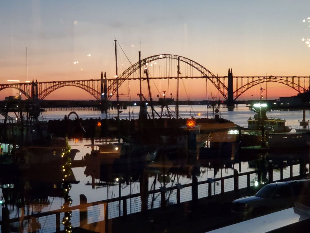 The view of the bridge over the bay in Newport at sunset from the window inside the restaurant. There are boats docked in the bay.