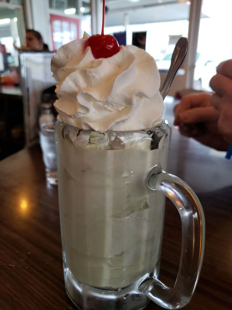A milkshake in a tall glass topped with whip cream and a cherry.