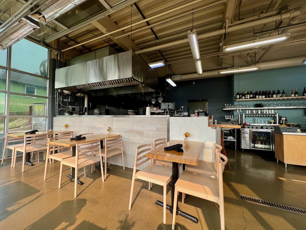 The modern interior of Local Ocean. There are light wood tables and chairs, and light green walls. There is lots of natural light coming in through the windows.