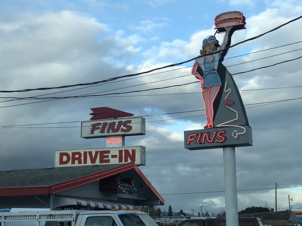 A retro sign of a woman holding a burger outside Fins.