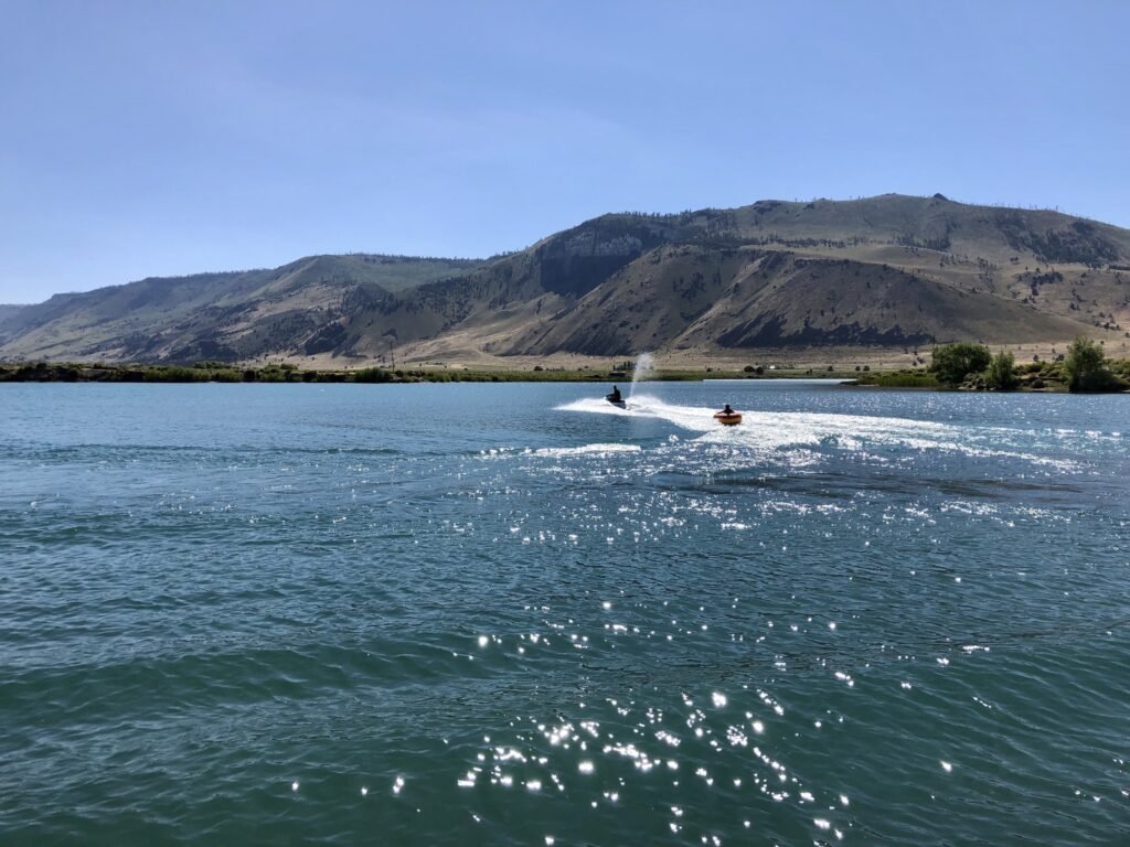 People on jetskis enjoying the waters of the Ana Reservoir on a blue sky day with no clouds.