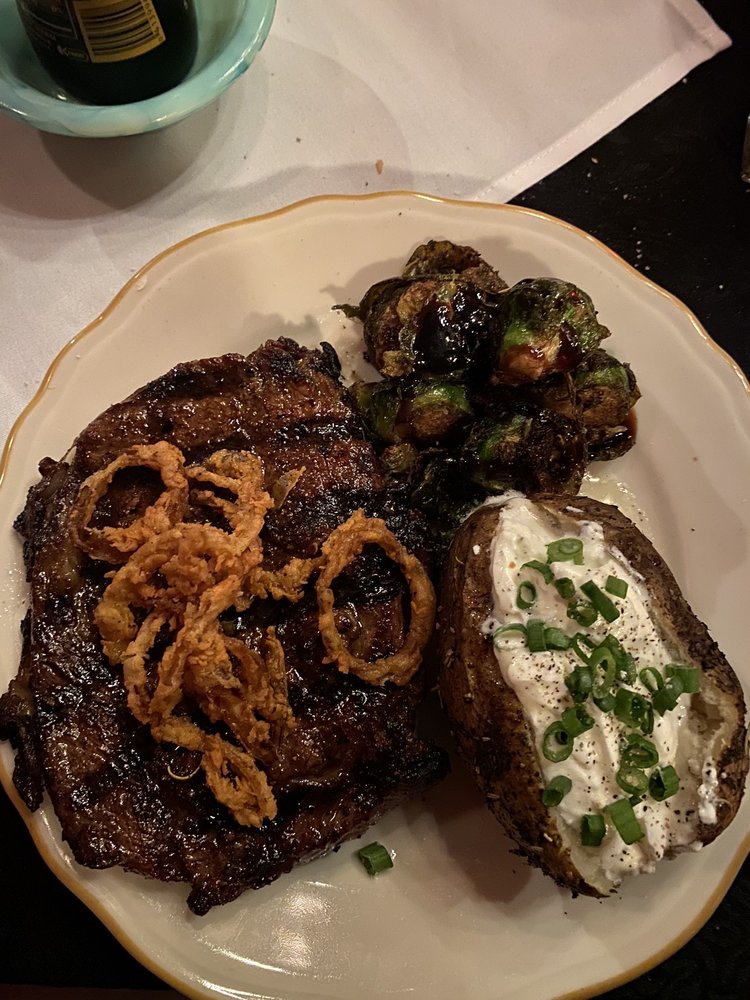 Ribeye with fried onions on top, a baked potato covered in chives, and seared brussel sprouts. Looks really good!