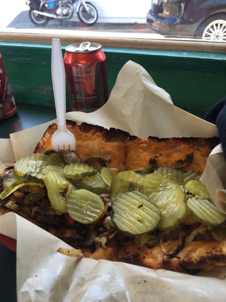 A huge sandwich lying open with toasted bread and lots of pickles on top.