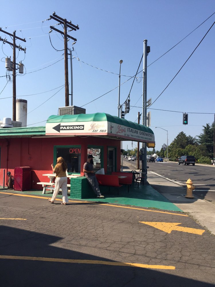 The outside of Luigi's. It's a small red building with a green roof and green painted small outdoor seating area.