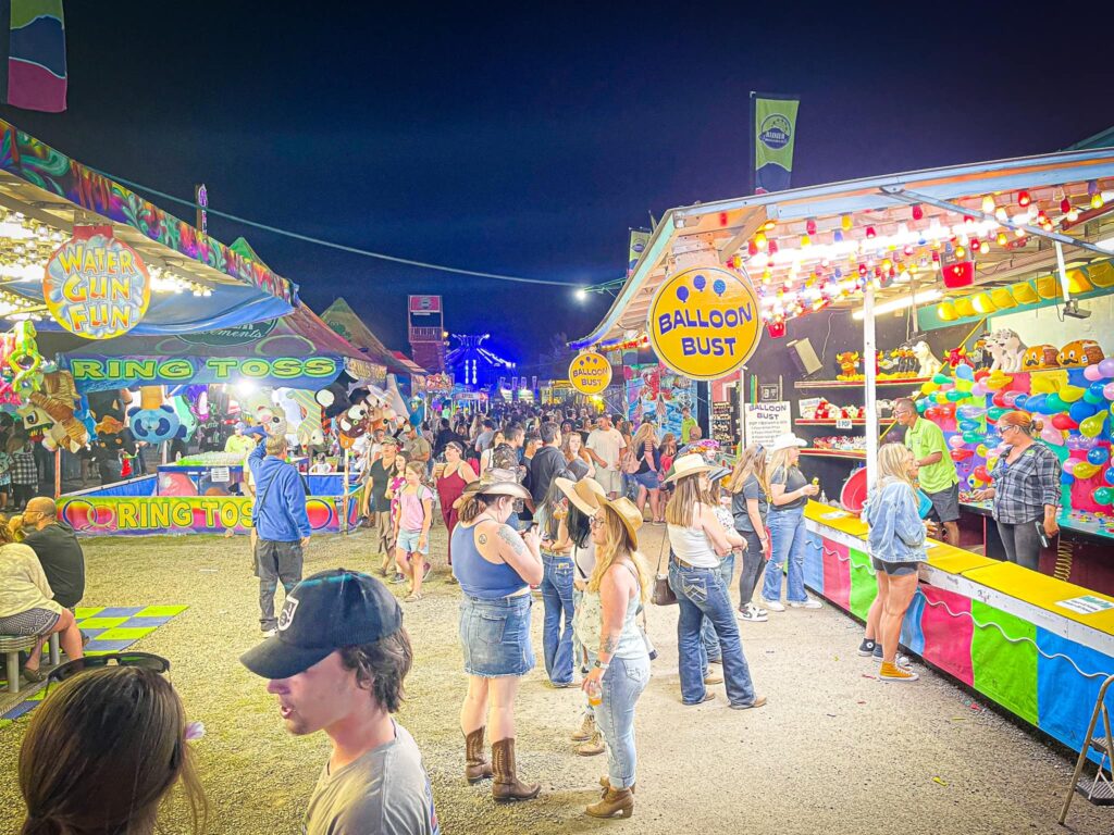 Brightly colored carnival games at the fair at night time.