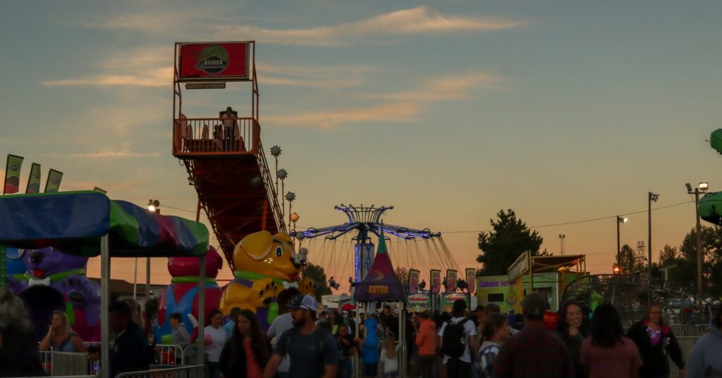 A carnival at sunset with carnival rides and a crowd of people.