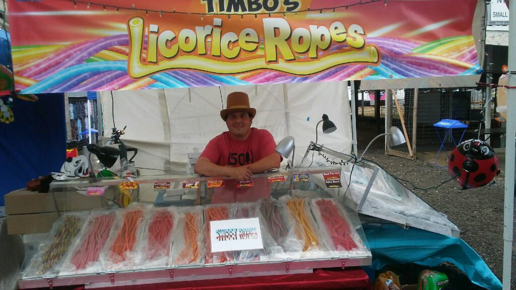 A man poses at his licorice rope stand at the county fair.