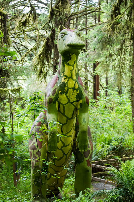 A tall green dinosaur sculpture emerges from the forest at the Prehistoric Gardens.