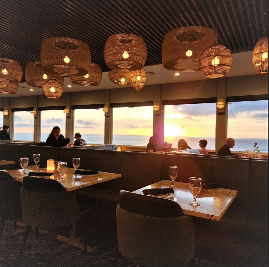 A view of the dining room at Georgie's. The furniture is nice and it has a view out large windows of the sunset and ocean.